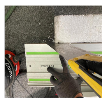 man cuts white polystyrene board with a stanley yellow hand saw