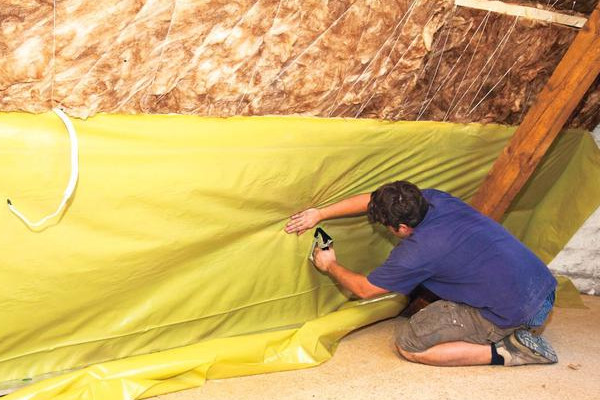 man installing yellow vapour control membrane on loft